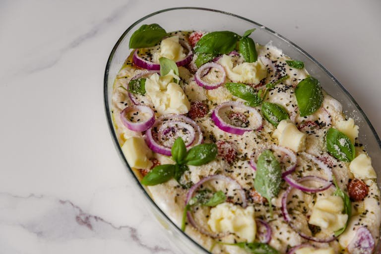 Tasty homemade baked casserole with cheese, onions, and fresh basil on a marble table.